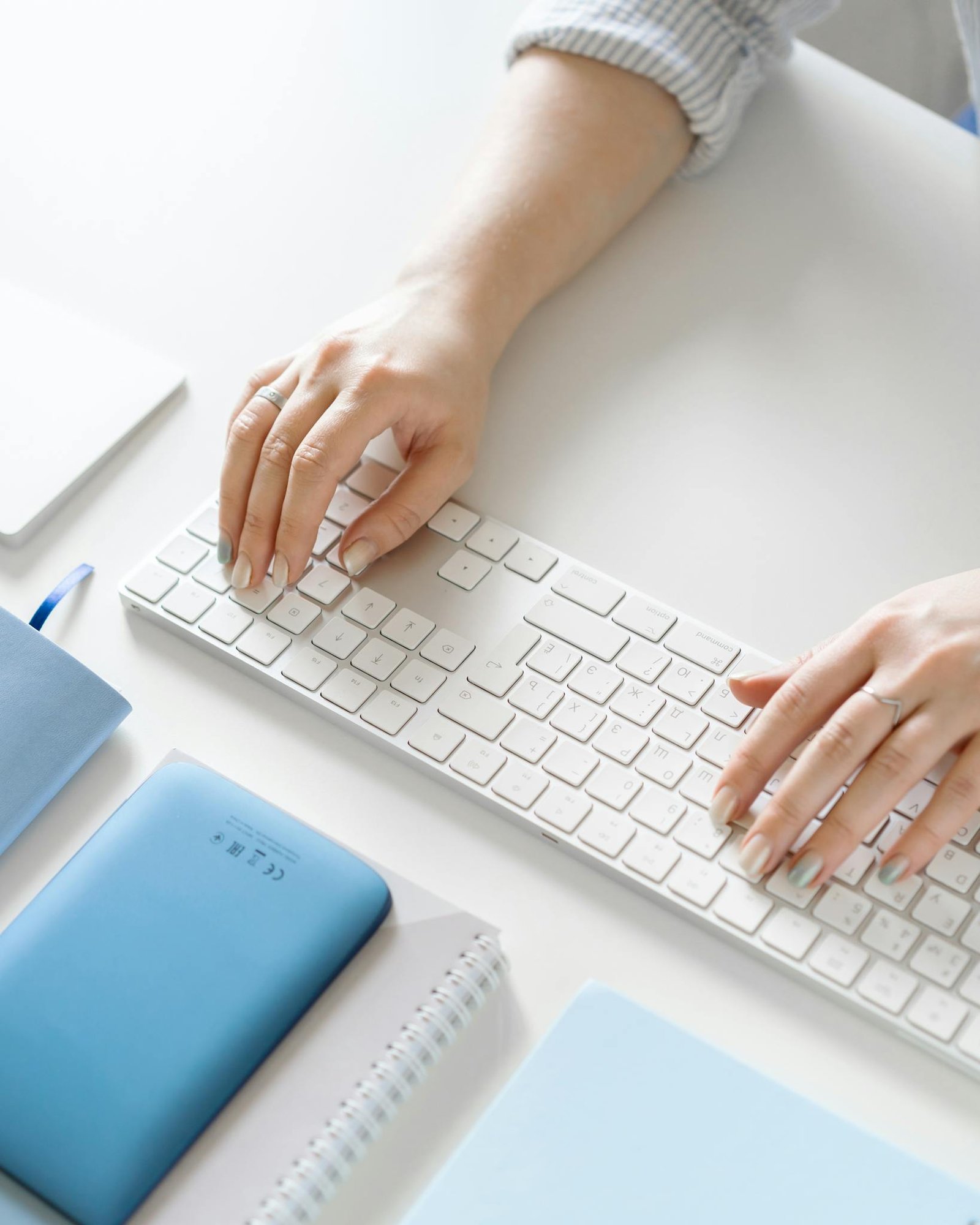 High-angle view of a person typing on a sleek keyboard with office supplies nearby, ample copy space.