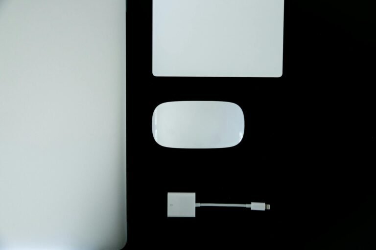Sleek flat lay of laptop, mouse, adapter, and notebook on black and white surface.
